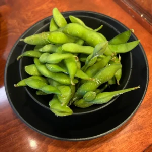 A black bowl full of edamame on a wooden table