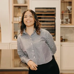 A young woman in a striped, button-down shirt leans against a counter and smiles